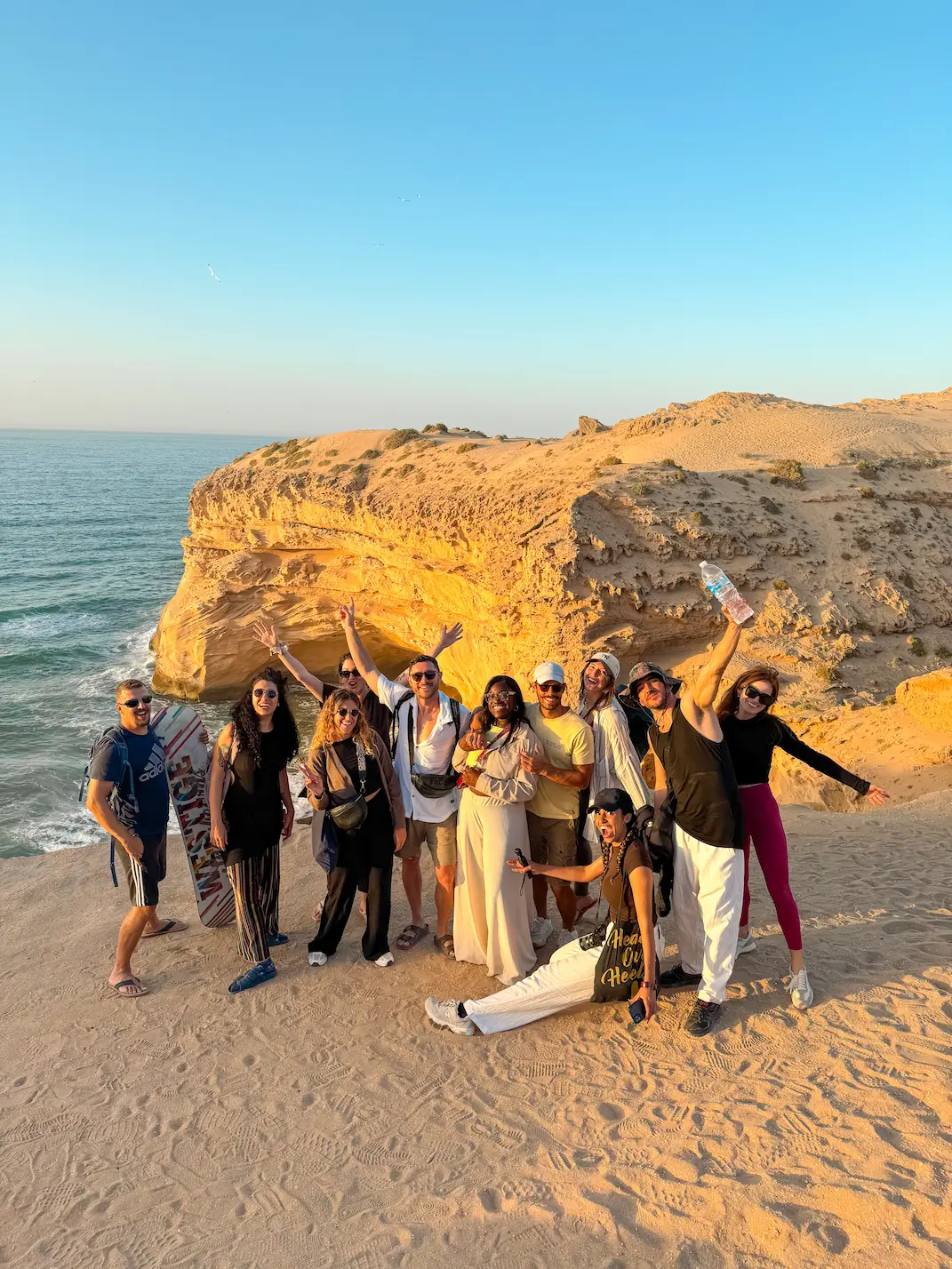 Mate group posing together with raised arms on sandy cliffs by the sea at sunset